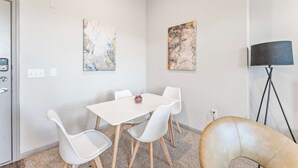Een moderne kamer met een witte tafel, vier witte stoelen, een zwarte vloerlamp en twee abstracte schilderijen aan de muur.
