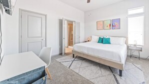 Een slaapkamer met een bed, een bureau, een stoel, een plafondventilator en een deur.