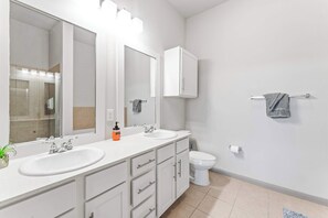 A modern bathroom with two sinks, a large mirror, a cabinet, and a toilet.