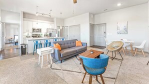Een moderne woonkamer met een grijze bank, blauwe stoelen, een houten salontafel en een plafondventilator.
