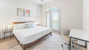 Une chambre à coucher comprenant un lit, un bureau, une chaise, un ventilateur de plafond et une fenêtre avec des stores.