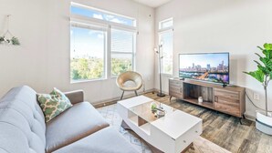 Un salon moderne avec un canapé, une table basse, un téléviseur et de grandes fenêtres.