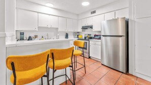 Una cocina moderna con armarios blancos, un refrigerador de acero inoxidable y dos taburetes amarillos.