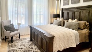 Ein Schlafzimmer mit einem großen Bett, einem Sessel, einer Chandelier und Kunstwerken an der Wand.
