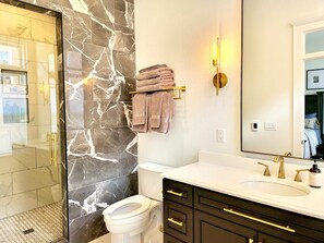 Ein modernes Badezimmer mit Marmorfliesen, einer weißen Toilette, einem Waschtisch mit goldfarbenem Wasserhahn und einem Handtuchhalter mit gefalteten Handtüchern.