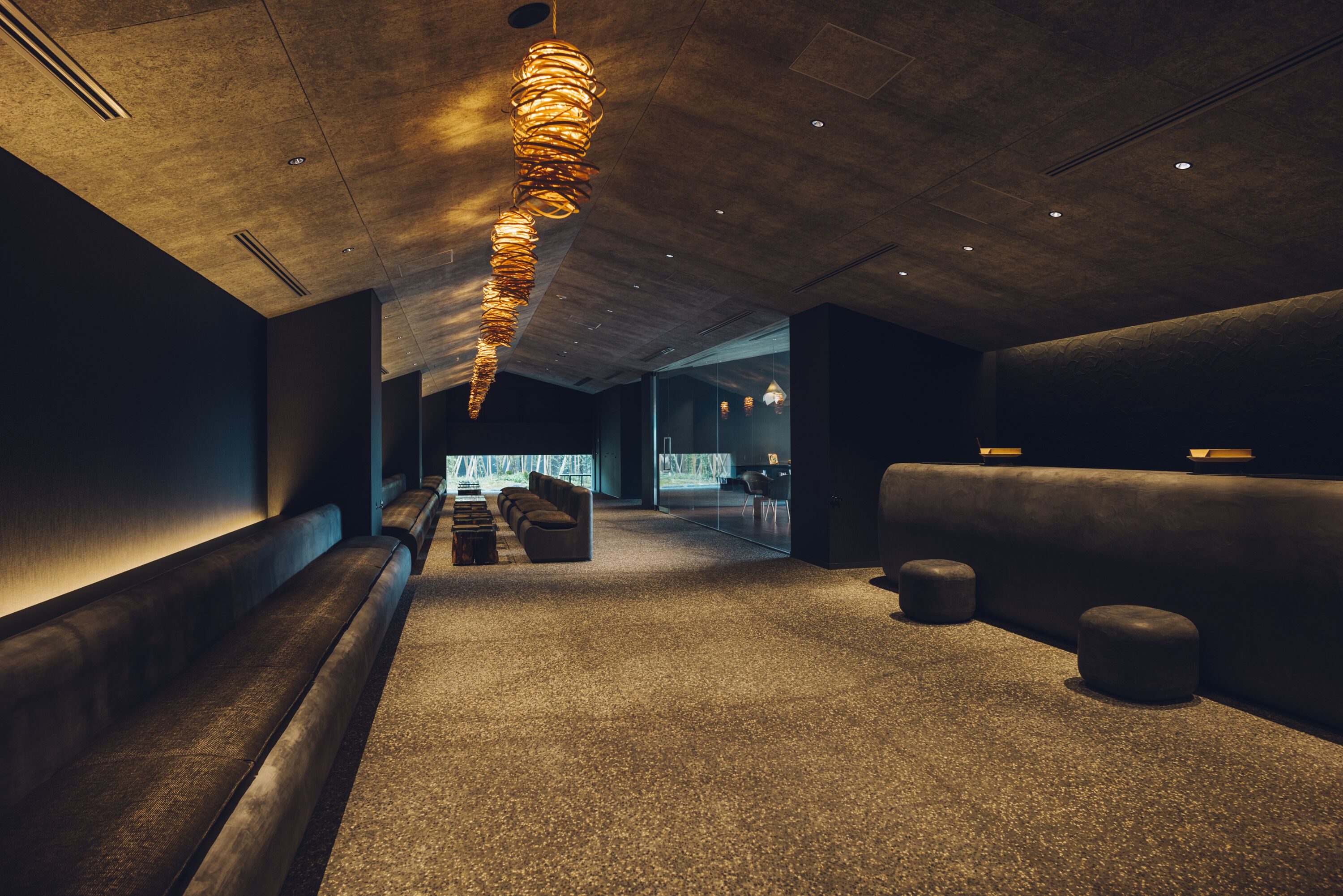 A modern interior with a long, curved light fixture, seating areas, and a glass partition in the background.