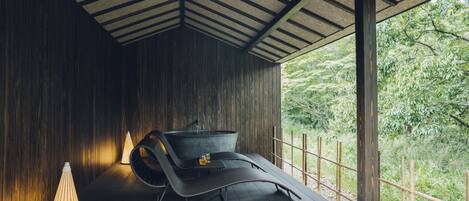 A modern, dark wooden room with a curved bench and a small table, a hanging light fixture, and a view of greenery outside.