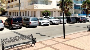 Ein mehrstöckiges Gebäude mit Balkonen, geparkten Autos und einer Bank im Vordergrund.