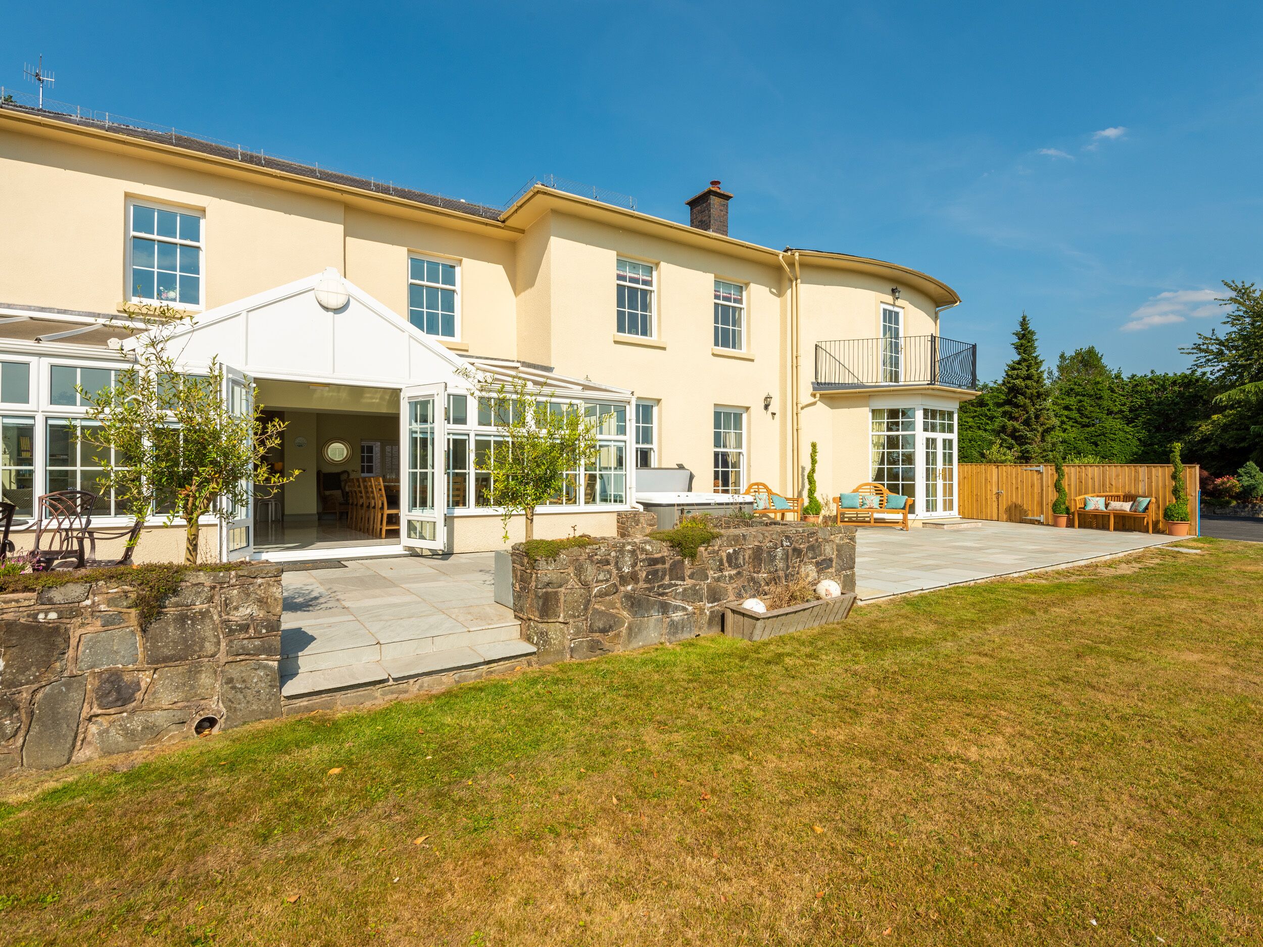 A two-story house with a covered patio, stone retaining wall, and a fenced backyard.