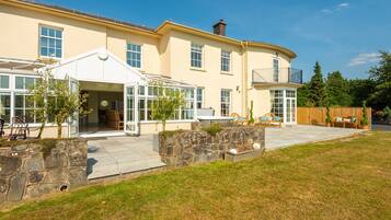 A two-story house with a covered patio, stone retaining wall, and a fenced backyard.