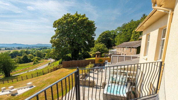 A balcony with a view of a swimming pool, a wooden deck, and a stone pathway.