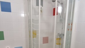 Un baño con ducha envuelta en vidrio, inodoro, lavabo y una alfombra marrón en el suelo.