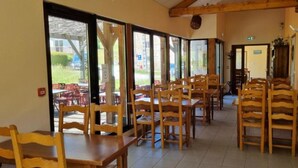 Comedor con mesas y sillas de madera, ventanas amplias y vistas al exterior.