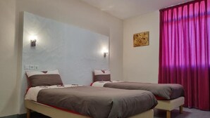 Una habitación con dos camas, una lámpara de pared, una obra de arte pequeña y una cortina roja.
