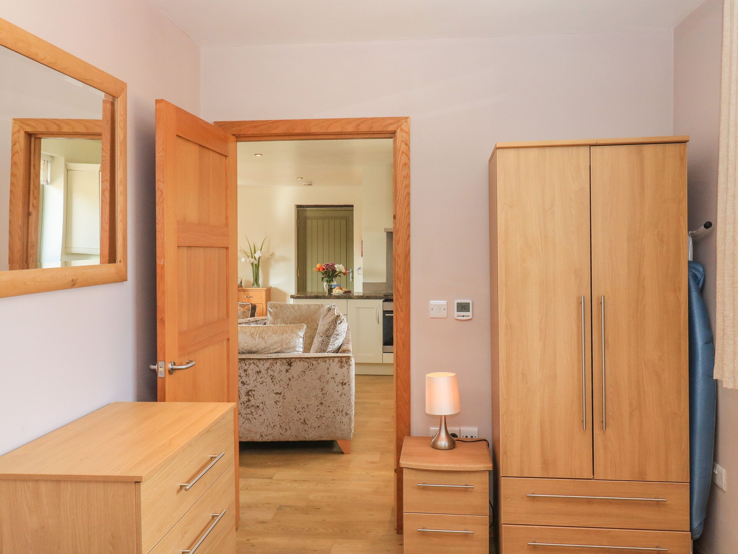 A hallway with a wooden wardrobe, a small bedside table with a lamp, and a sofa in the background.