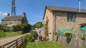 A stone building with a sloped roof, a wooden fence, and a grassy yard. - The Mews (Newton Abbot)