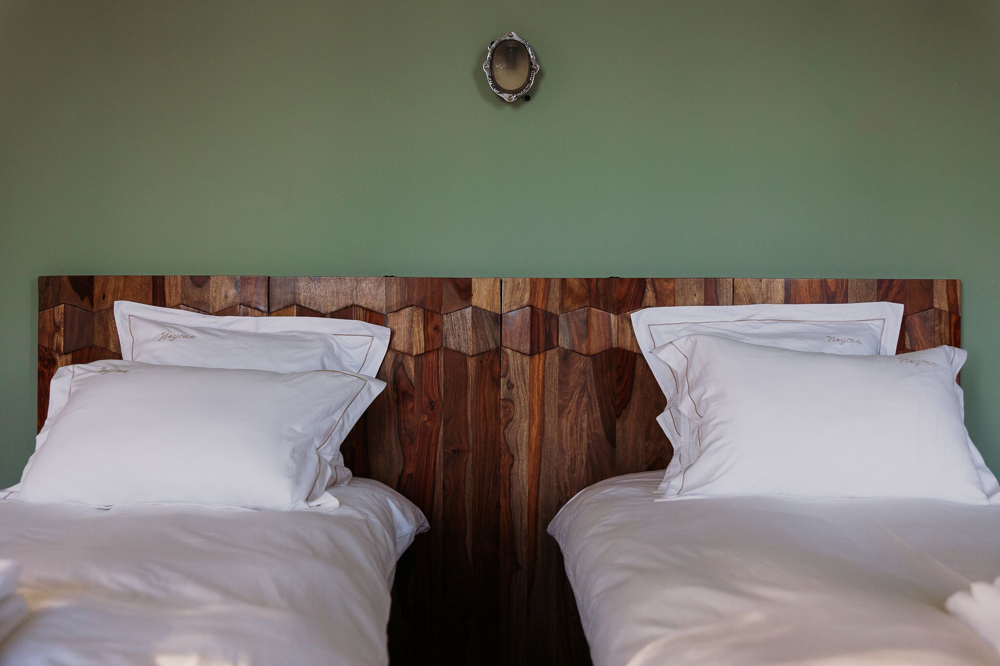 Une chambre avec deux lits, une tête de lit en bois et un mur vert.