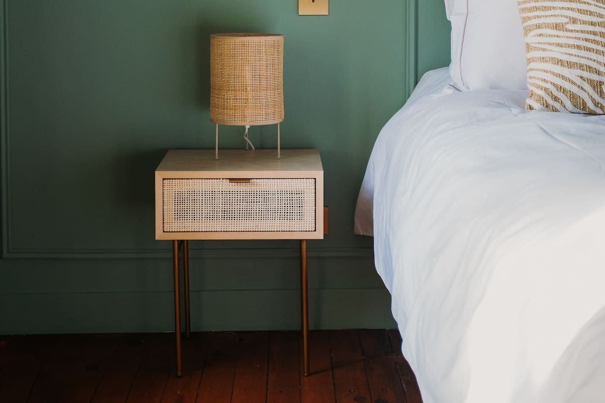 Une chambre avec un mur vert, une table de chevet avec une lampe et un lit avec une literie blanche.