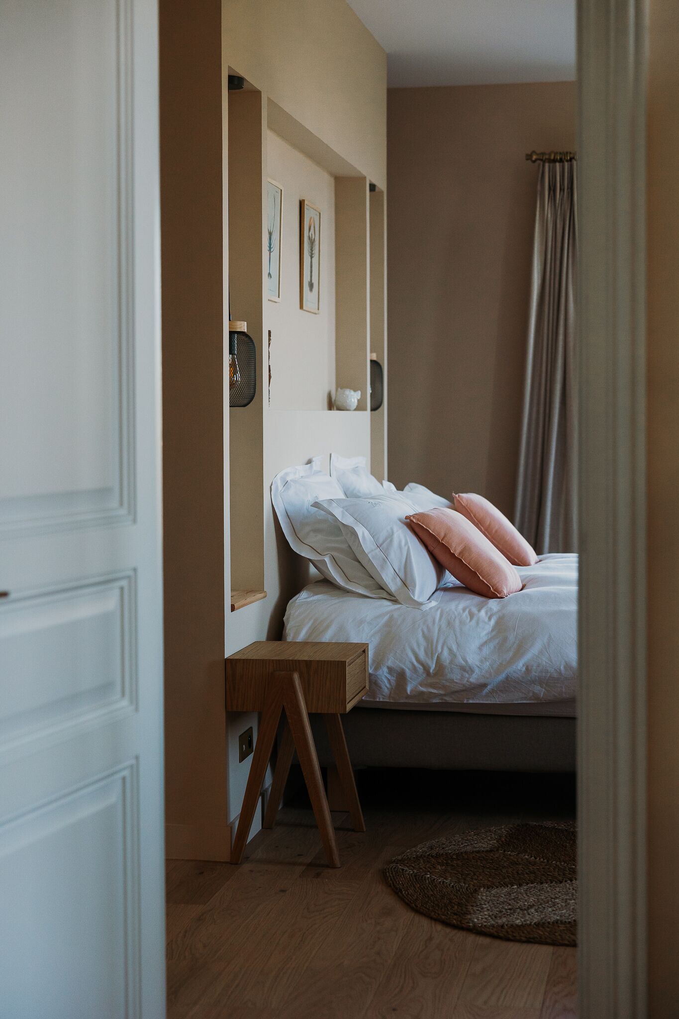 Une chambre à coucher avec un lit, une table de chevet, un plancher en bois et une étagère murale ornée de tableaux.