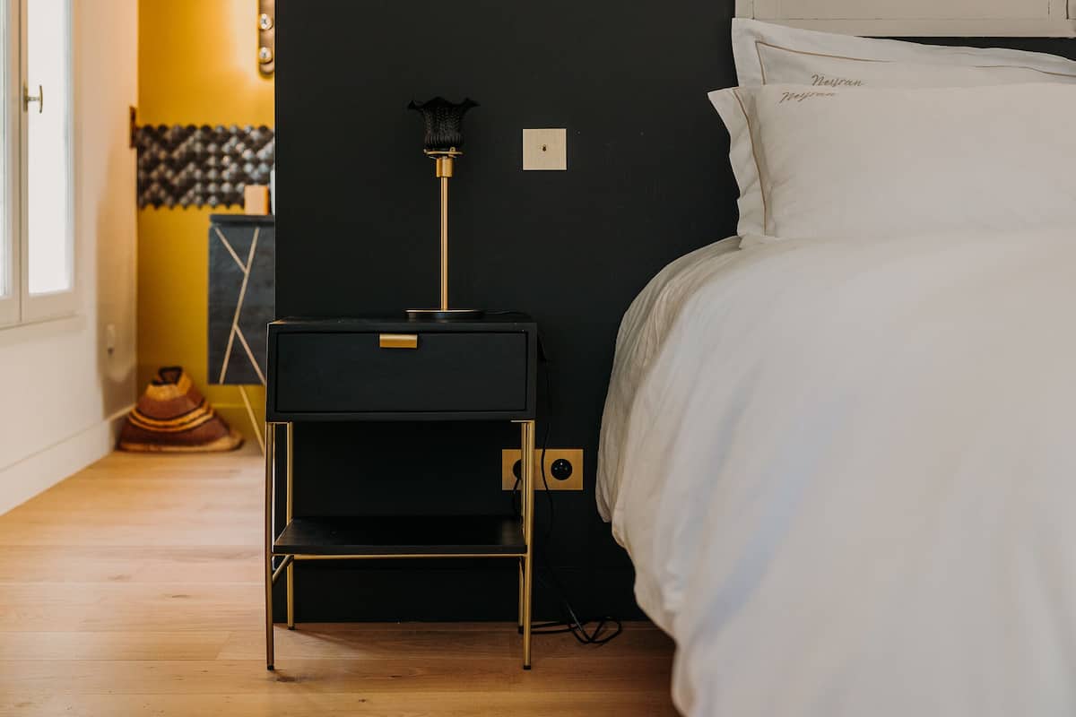 Une chambre à coucher avec une table de chevet noire, une lampe et un lit recouvert de linge de lit blanc.