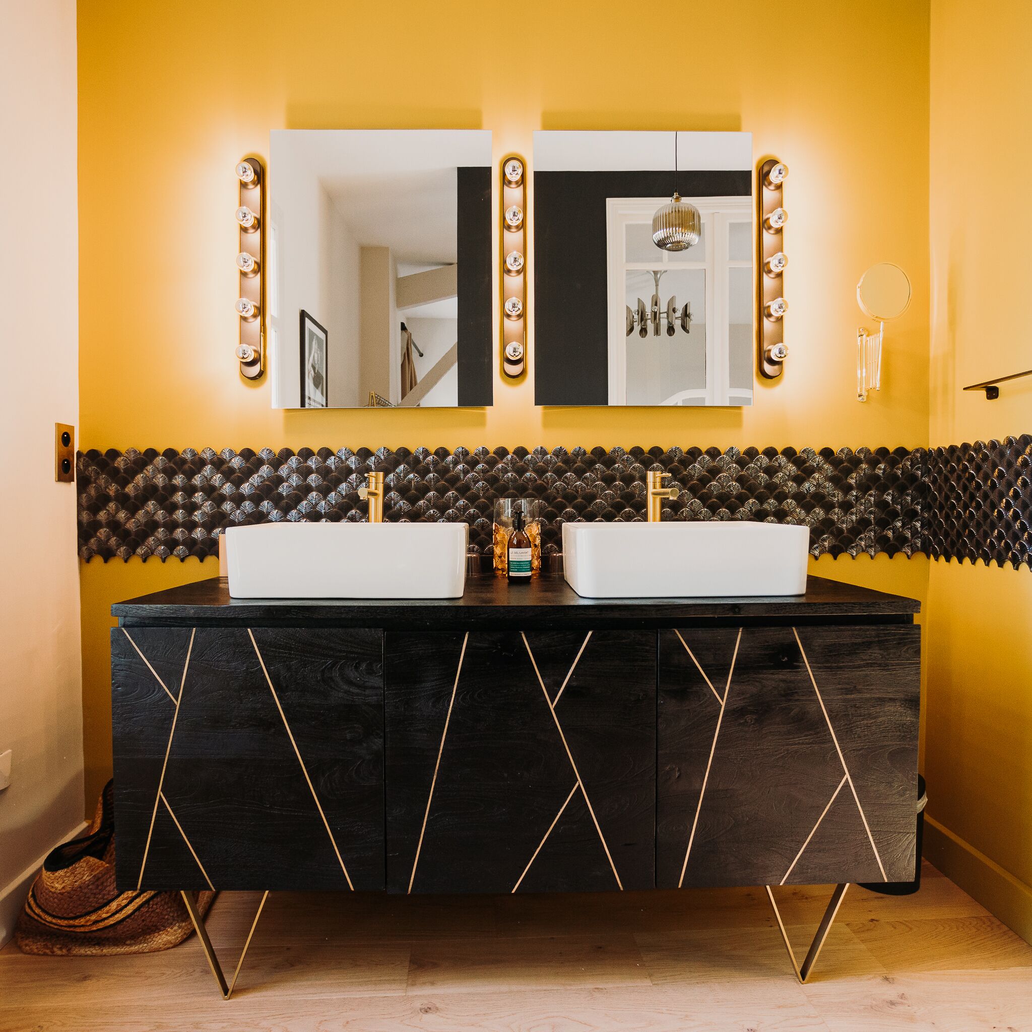 A bathroom with a black vanity, two sinks, and a mirror with lights.