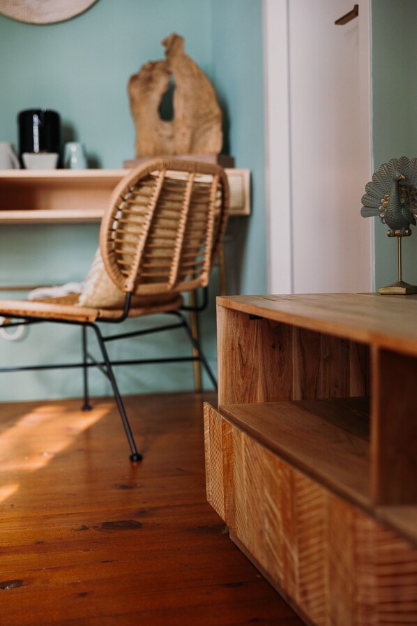Una habitación con una silla de mimbre, muebles de madera y un estante en la pared con un hervidor.