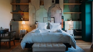 Quarto bem arrumado com cama grande, mesas de cabeceira, uma cadeira e parede com design exclusivo em formato de garrafa.