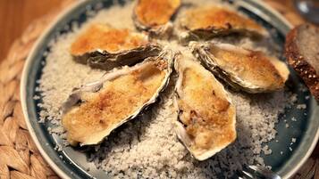 Een bord met oesters op hun schaal, bestrooid met grof zout, een vork en een glas witte wijn op een geweven mat.