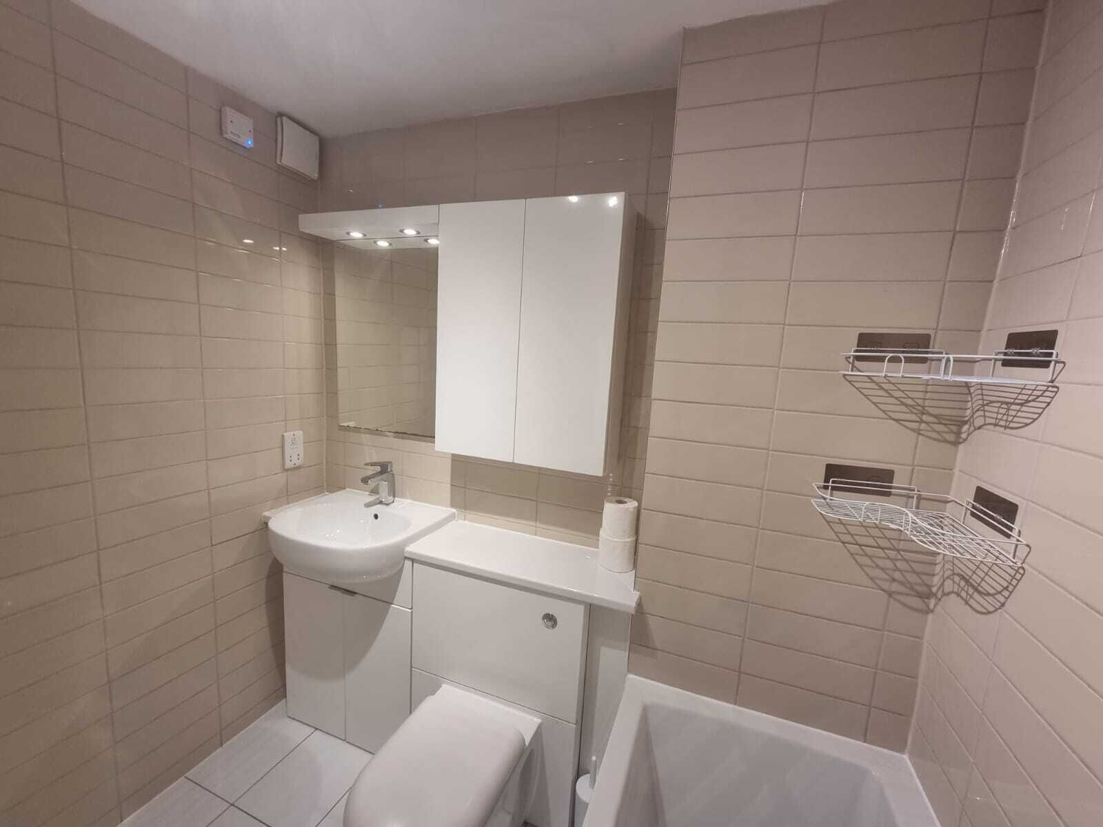 Ein modernes Badezimmer mit Waschbecken, Spiegel und Toilette in Weiß, sowie eine Badewanne mit integrierten Ablagen.