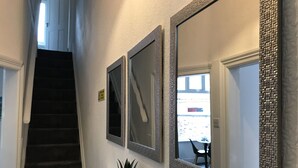 A hallway with three mirrors on the wall, a staircase, and a potted plant on a white console. - Bright Spacious 3-bed With Office & Patio, Preston (Preston)