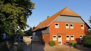 Un edificio in mattoni di due piani con tetto a falde, diverse finestre e un cortile recintato.