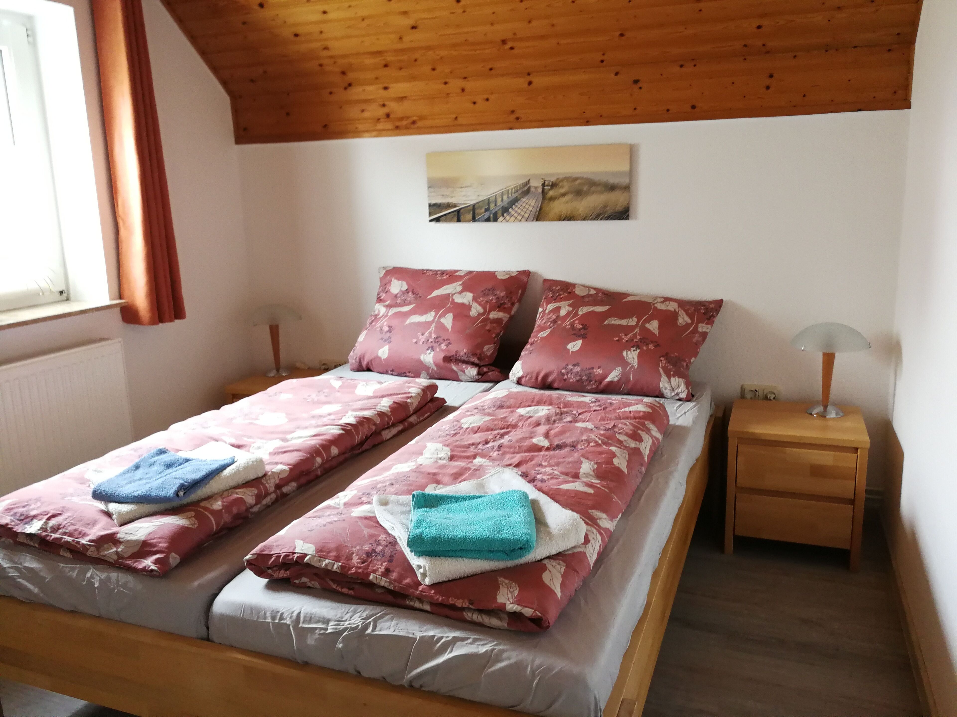 Ein Doppelbett mit floralem Bettbezug, ein Nachttisch mit Lampe und ein Gemälde an der Wand.