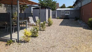 Un patio coperto con tavolo e sedie, un piccolo deposito e un vialetto sterrato.