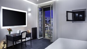 Una habitación de hotel moderna con una cama grande, un escritorio con silla, un ventanal con vistas a la ciudad y un televisor de pantalla plana montado en la pared.