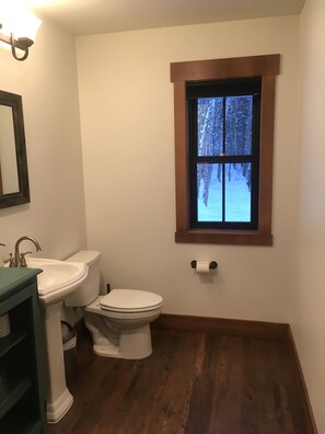 Une salle de bain équipée d’un lavabo, de toilettes et d’une fenêtre donnant sur un paysage enneigé.
