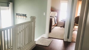 A hallway with a white railing, a welcome sign, a carpeted floor, and a bed in the background. - Cute cozy apartment. Half a block walking distance from beautiful downtown Ionia (Ionia)