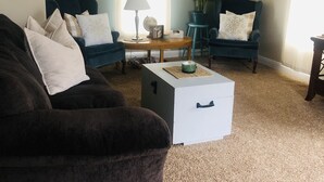 A living room with a dark brown sofa, a white coffee table, and two blue armchairs. There is a lamp on a wooden side table, and a potted plant. - Cute cozy apartment. Half a block walking distance from beautiful downtown Ionia (Ionia)