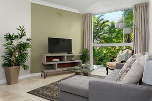 A living room with a sofa, a glass coffee table, a TV on a stand, and a large window with curtains. - Sonwyk 9 (Cape Town)