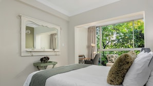 A bedroom with a large bed, a vanity with a mirror, a window with a view of trees, and a desk with a chair. - Sonwyk 9 (Cape Town)