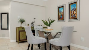A dining area with a glass table, two upholstered chairs, a green cabinet, and two framed paintings on the wall. - Sonwyk 9 (Cape Town)