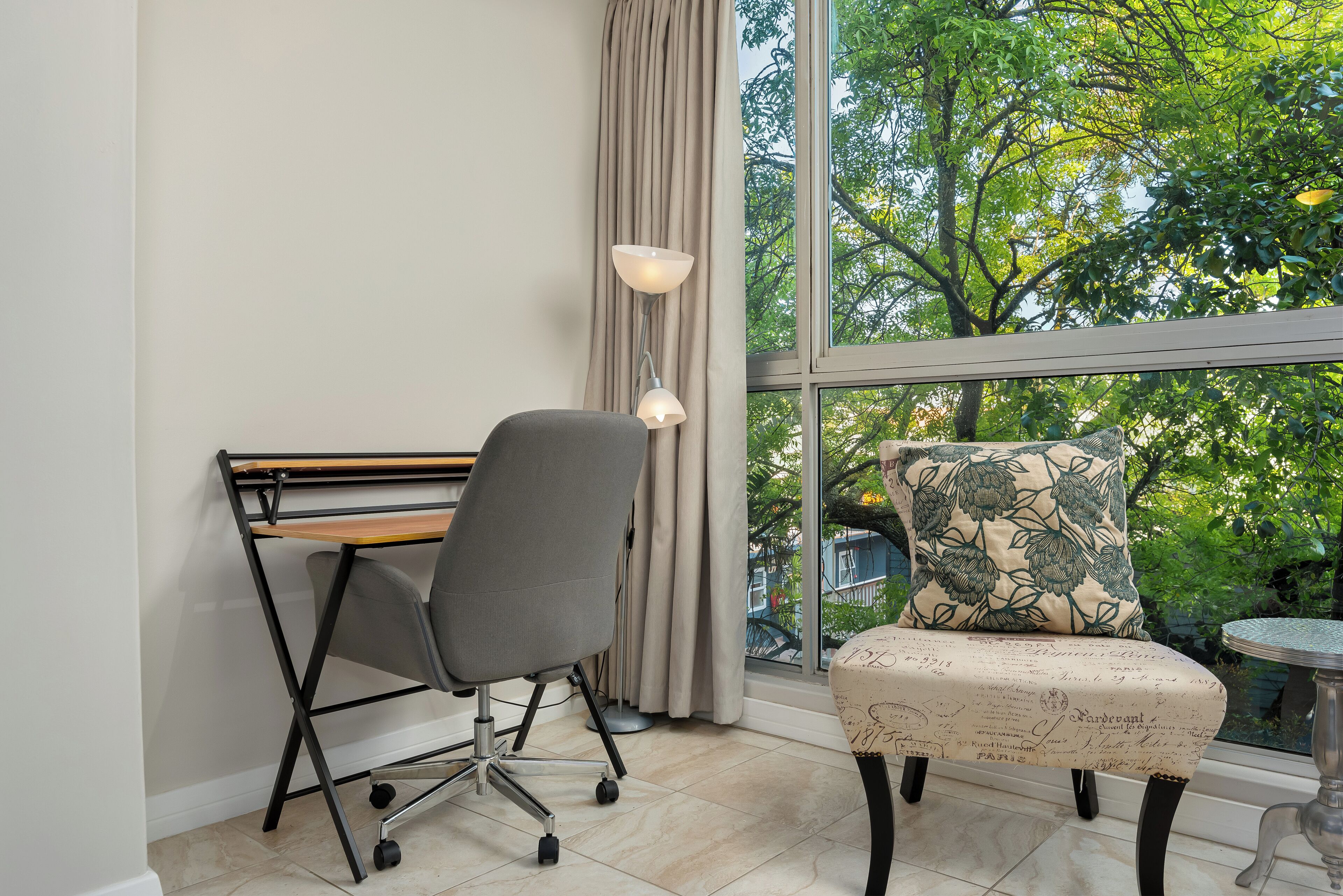 Ein modernes Zimmer mit Schreibtisch, Stuhl und Blick auf Bäume durch ein großes Fenster.