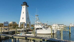 A lighthouse and a dock with boats, a clear sky, and a marina in the background.