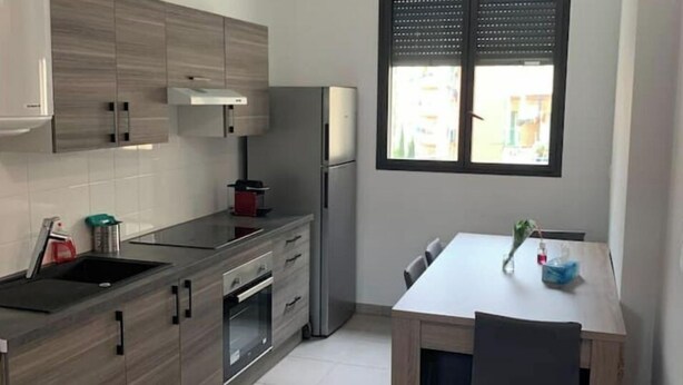 Et moderne køkken med grå skabe, et rustfrit stål køleskab og et spiseområde med et bord og stole.