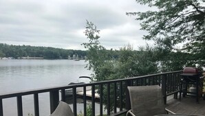 En træterrasse med udsigt over en sø, en båd ligger til anker, og udendørs møbler.
