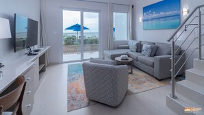 Una sala de estar moderna con un televisor de pantalla plana, un sofá gris, un taburete estampado y una escalera.