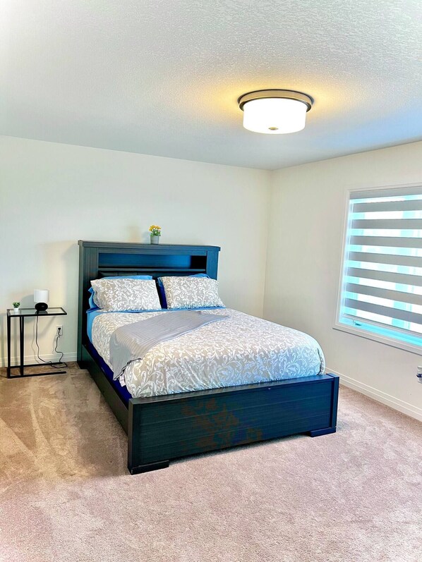A bedroom with a bed, a nightstand, a lamp, a window with blinds, and a ceiling light.
