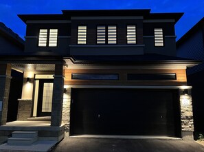 Stunning two-story residence with a prominent garage and stone base, featuring a flat roof with windows and a well-lit entrance.