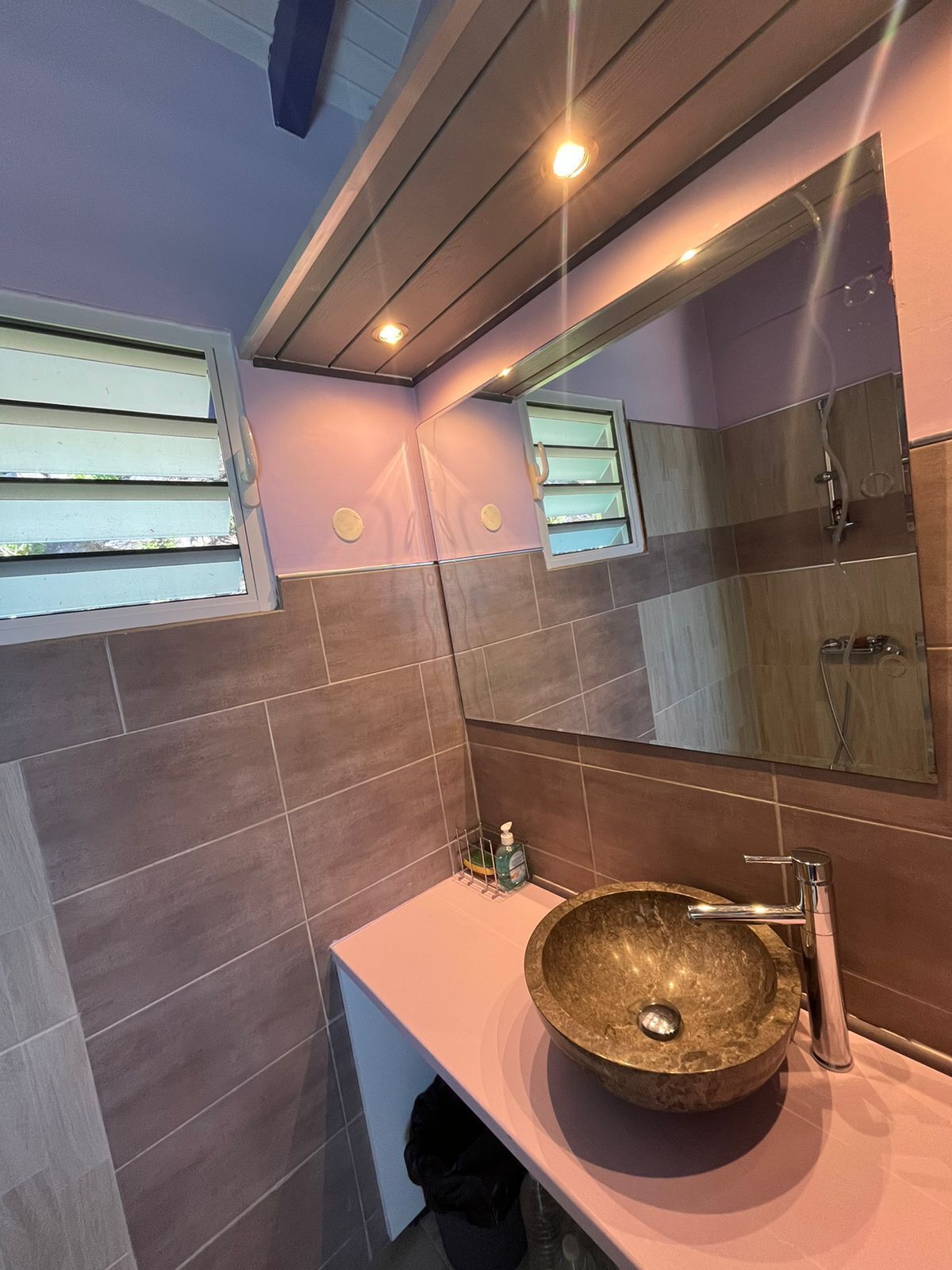 Une salle de bain moderne avec un grand miroir, un lavabo rond et une fenêtre équipée de stores.