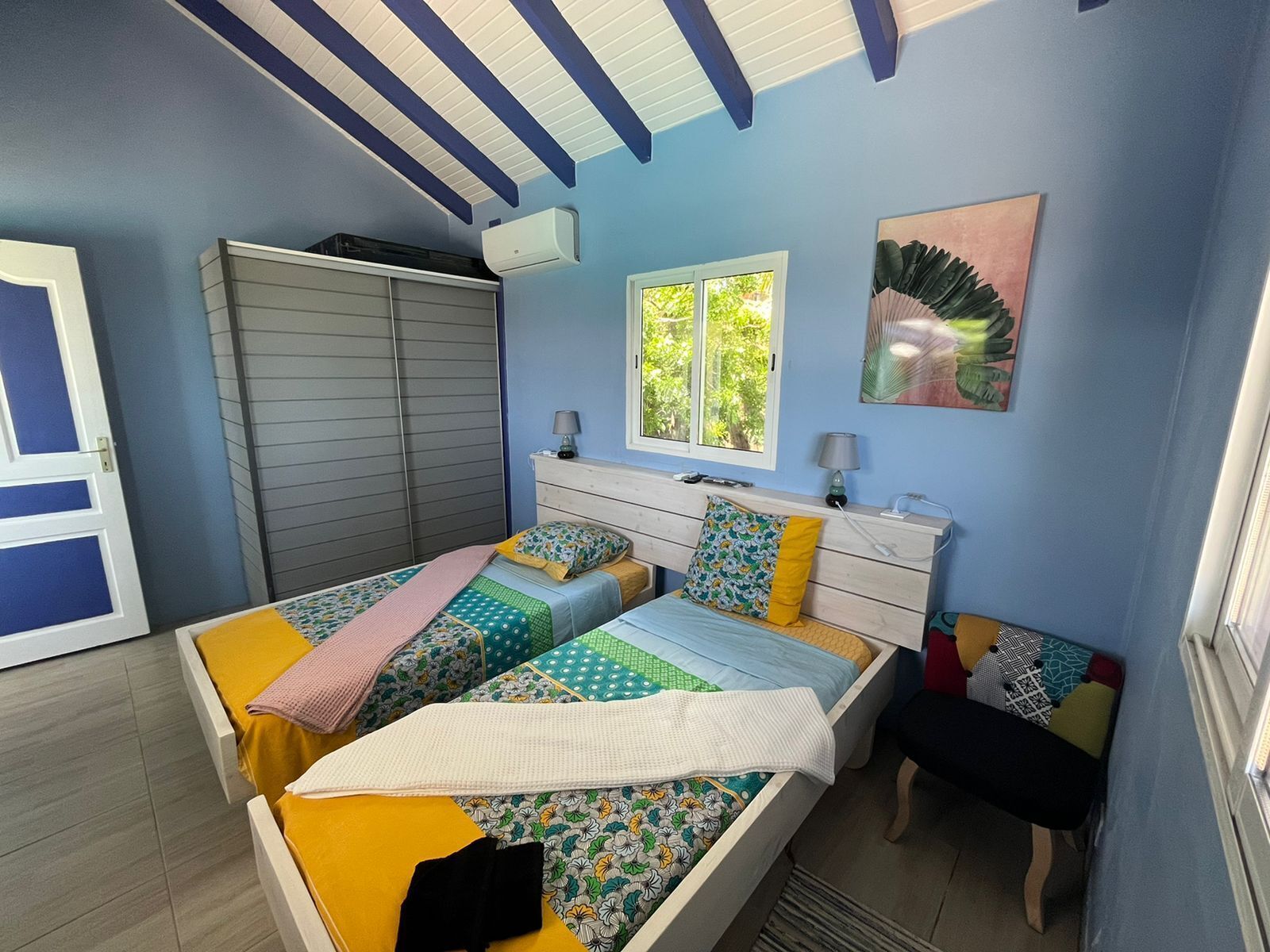 Un dormitorio con cama, mesitas de noche, armario, ventana y un cuadro en la pared.