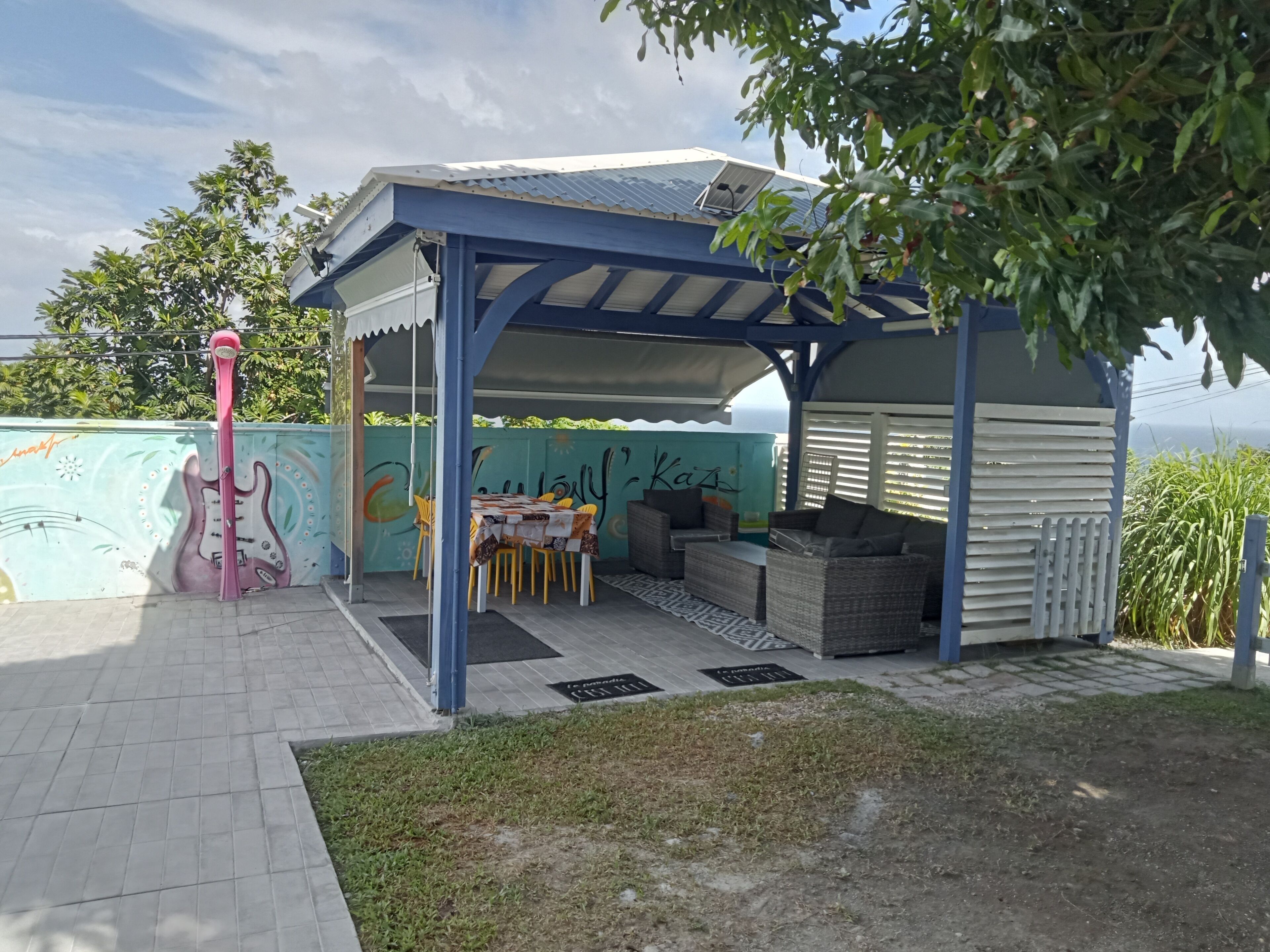 A covered outdoor seating area with a table and chairs, a pink flamingo decoration, and a mural on the wall.